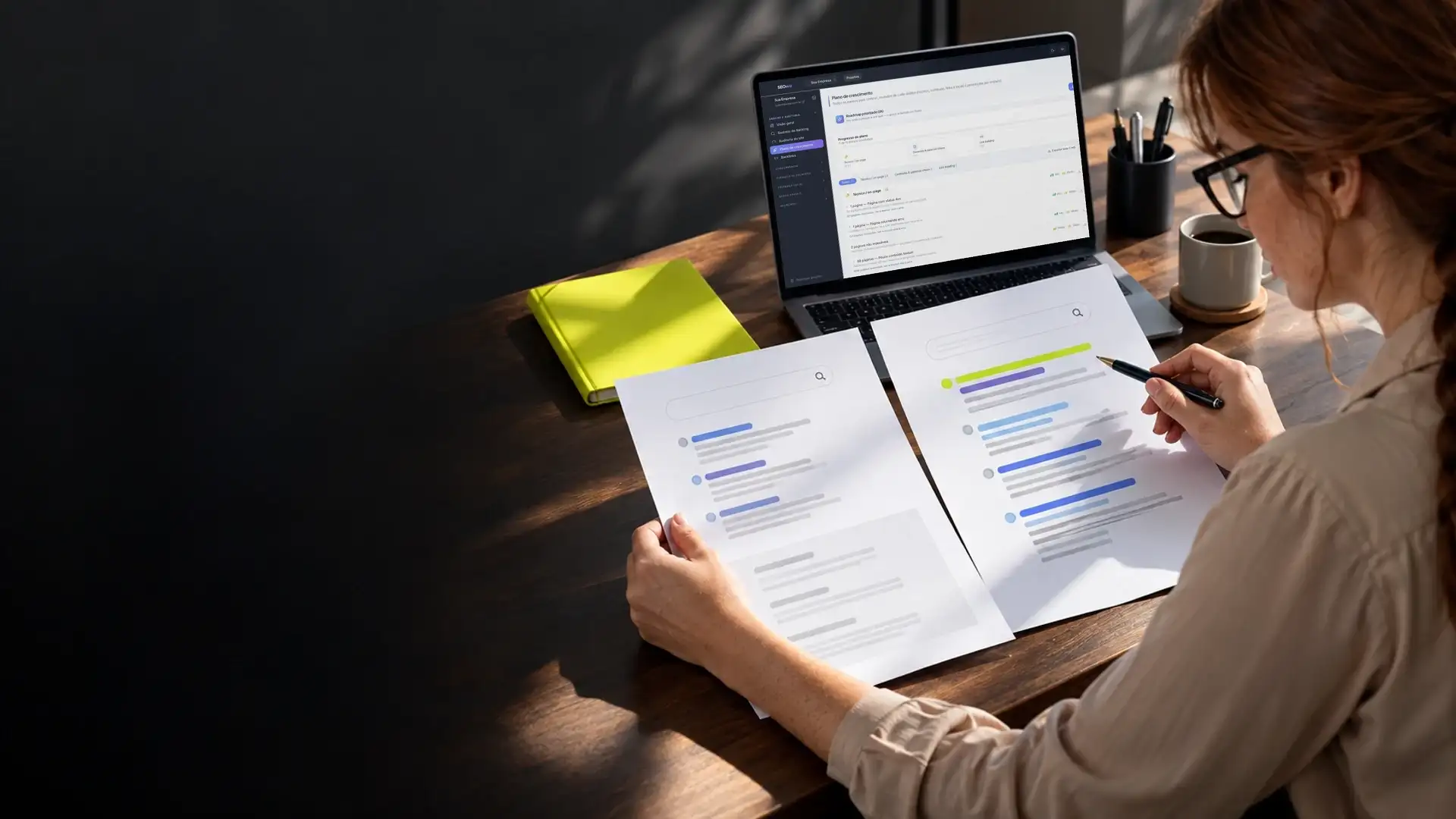 Mulher comparando duas páginas impressas de resultados do Google, com o painel de SEO aberto no notebook